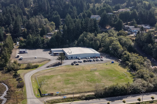 Coos Bay, Oregon, United States - 11 September 2026: Aerial view of the Pepsi facility, featuring a warehouse, delivery trucks in the lot, and surrounding forest.