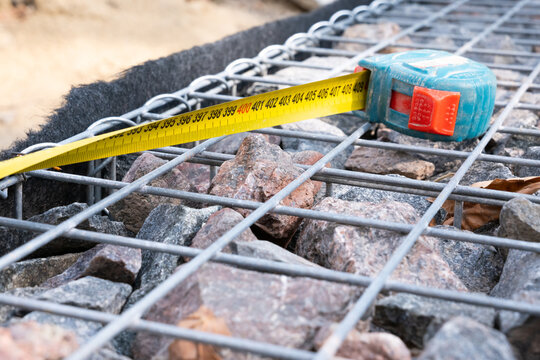 Yellow measuring tape on steel wire mesh gabion wall filled with stones at construction site