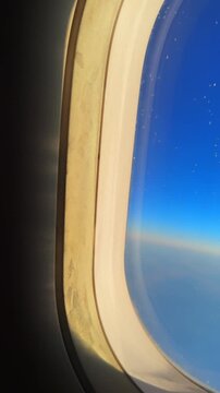 View through an airplane window showcasing a bright blue sky and sunlight at sunrise or sunset
