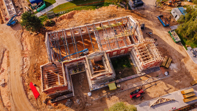 Valmiera, Valmiera Municipality, Latvia - 09 September 2026: Aerial view of a building under renovation with exposed wooden roof trusses, brick walls, and construction equipment on a dirt site.