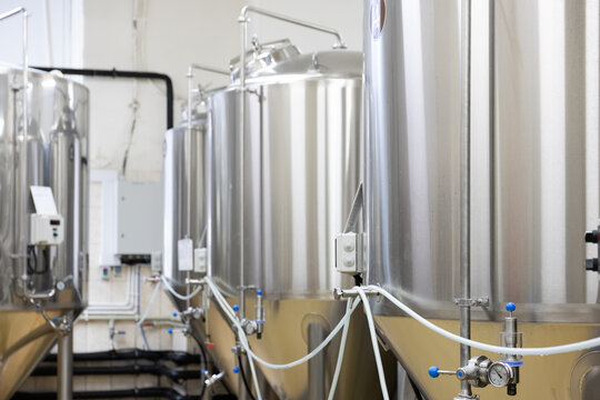 Row of stainless steel fermentation tanks with pipes and valves inside brewery