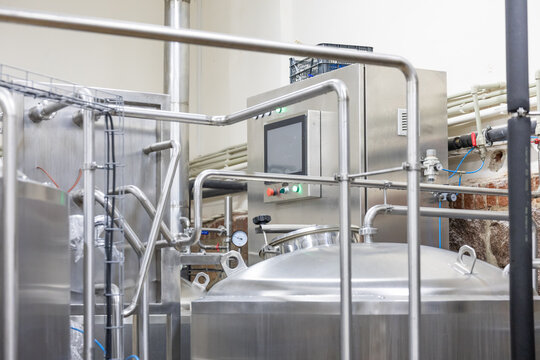 Stainless steel brewery tanks with pipes and control panel inside production facility