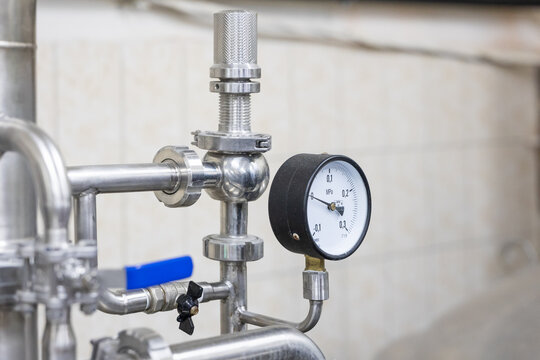 Close up of pressure gauge with stainless steel pipes and valves on brewery equipment