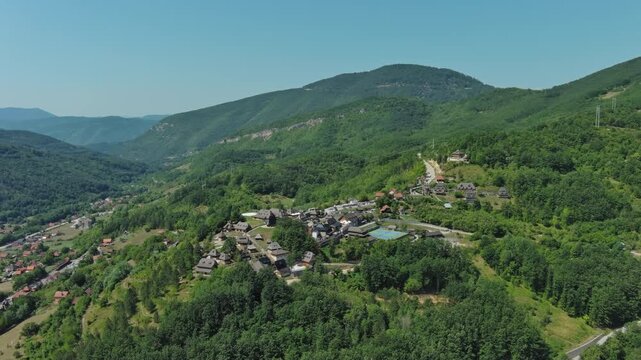 Aerial around view of Drvengrad Kustendorf ethno village on Mokra Gora, Serbia, surrounded by green hills and mountains, 4k