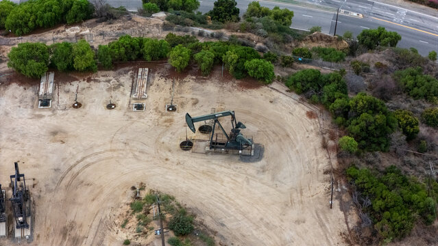 Aerial view of a pumpjack in the Baldwin Hills oil field, surrounded by dry terrain, sparse vegetation, and nearby roads in Los Angeles, California, United States.