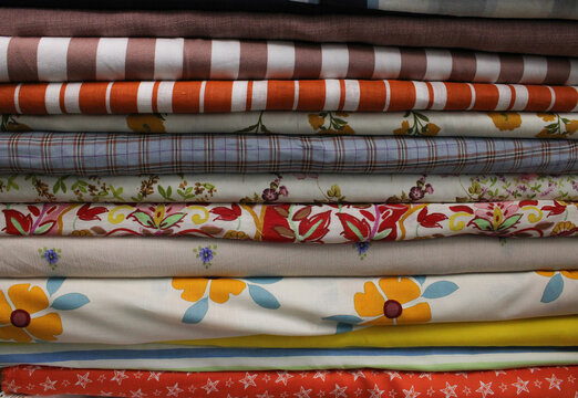 High-angle stack of colorful folded cotton fabrics with various patterns including floral, plaid, stripes, and stars.