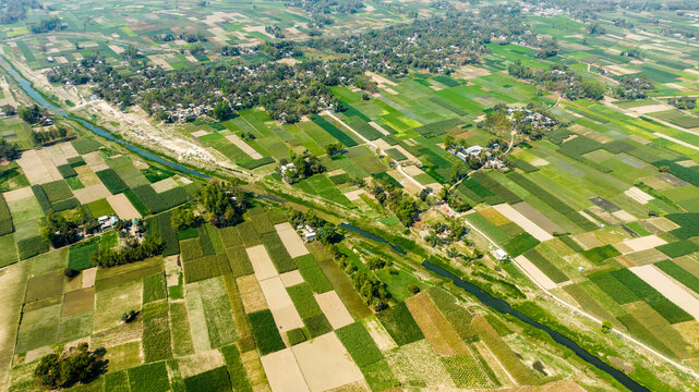 Aerial view of agricultural fields and a winding canal surrounded by rural houses and lush greenery in Manikganj, Dhaka Division, Bangladesh.