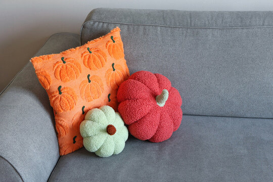 Decorative pumpkin pillows and a bright orange cushion lean together on a neutral gray sofa. Concept of autumn-inspired cozy decor.