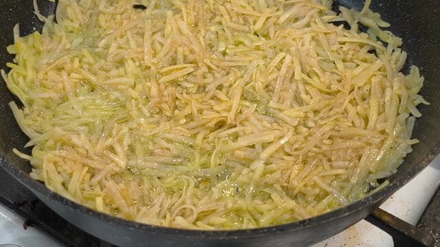 Large grated potato fritter cooking in a frying pan. Hot oil bubbles around the potato pancake as a golden crispy crust forms during frying. Homemade potato pancake made from coarsely grated potatoes.