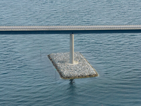 Aerial view of Lepsoy bridge spanning over deep blue waters, showing the concrete pillar supported by a stone foundation in Haram, More og Romsdal, Norway.