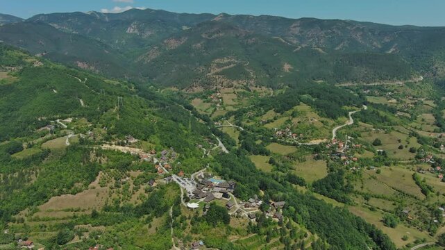 Aerial around view of Drvengrad Kustendorf ethno village on Mokra Gora, Serbia, surrounded by green hills and mountains, 4k