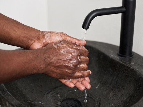 Person washing hands under a modern black faucet in a stone basin