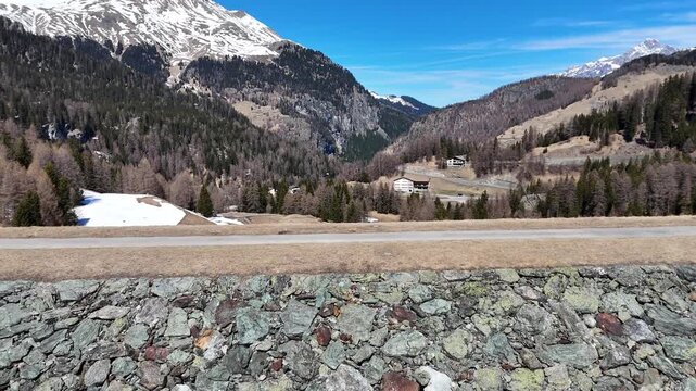 rockfill dam wall descends toward switchback road patchy snow blankets alpine meadow forested slopes hamlet rooftops marmorera resettled village snowcapped peaks julier pass graubunden switzerland
