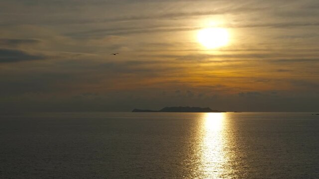 Golden sun setting over calm ocean water. Beautiful calm sea with the sun setting over the horizon, casting a golden reflection on the water. A solitary island sits in the distance