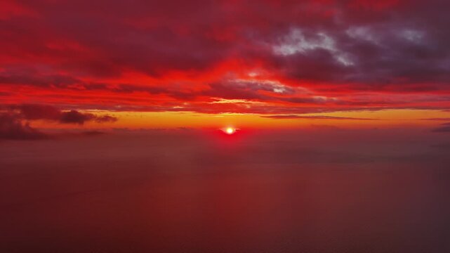 Aerial view of bright red sun setting over calm sea. Scenic view of ocean horizon with dramatic clouds. Natural landscape background, 4k