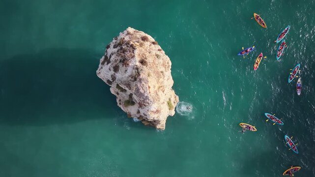Person jumping from cliff into turquoise water near kayaks