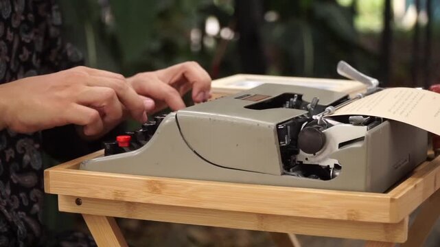 Side view of hands typing on a vintage mechanical typewriter set on a small wooden table outdoors