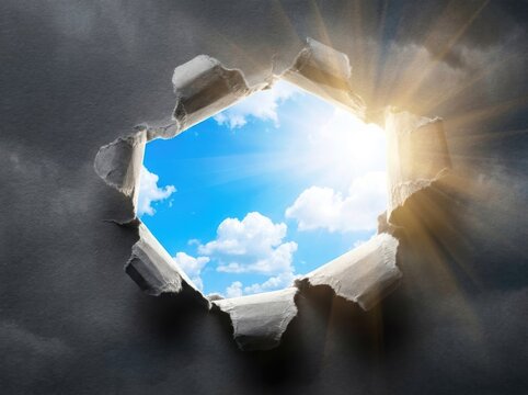 Torn paper effect revealing bright blue sky and sun rays through dark clouds