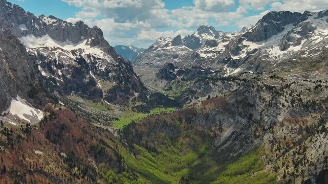 Aerial view of amazing rocky mountains in snow and green valley, Prokletie park, Montenegro and Albania, 4k
