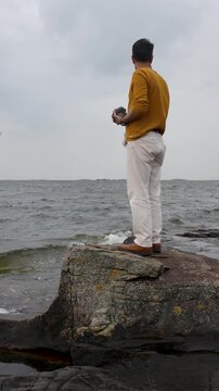 Man Throwing Stones Into the Sea on a Cloudy Day at the Beach