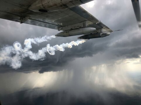 Cloud seeding aircraft wing releasing silver iodide flares into storm