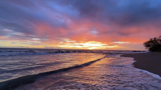 Waves crash on the shore as the sun sets in a vibrant sky at the beach. The atmosphere shows nature's beauty during twilight.