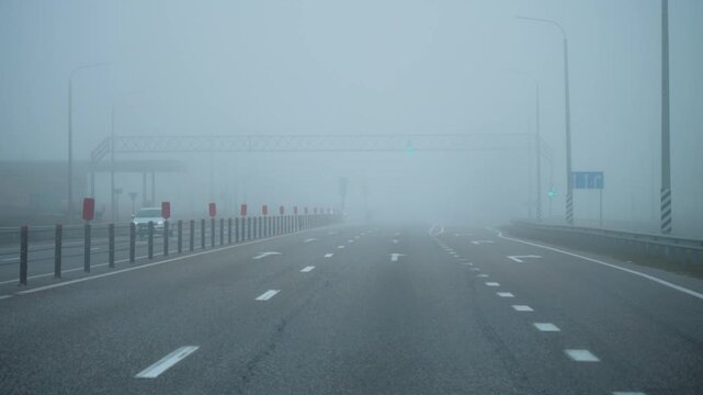Driving through dense fog on multi lane highway with very low visibility, road markings and traffic lights fading in mist, hazardous weather and road safety concept.