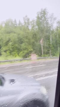 Blurred rainy road view from car window with tree lined highway and wet glass
