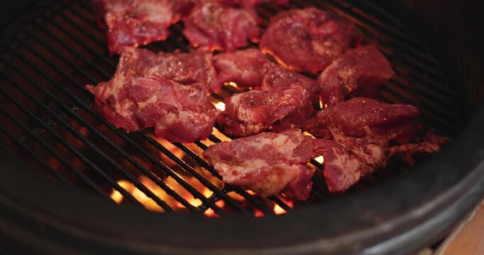 A man puts pieces of raw meat on the grill of a round grill, hot coals under the grill, and an egg-shaped grill.