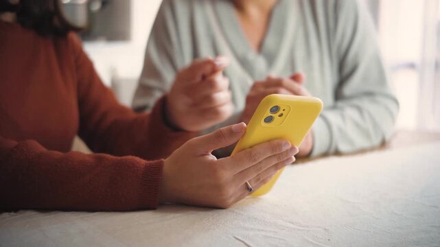 Anonymous young woman's hands teaching an adult how to use a smartphone, representing digital literacy, technology education, support, and intergenerational learning.
