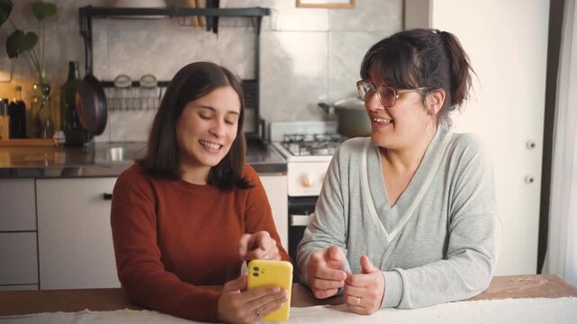 Young Latina woman at home teaching her mother how to use a smartphone, representing digital literacy, family support, technology education, and intergenerational learning.
