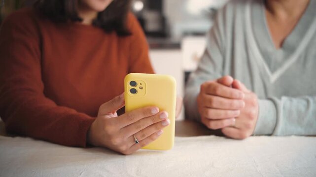 Anonymous young woman teaching an adult how to use a smartphone at home, representing digital literacy, technology education, support, and intergenerational learning.
