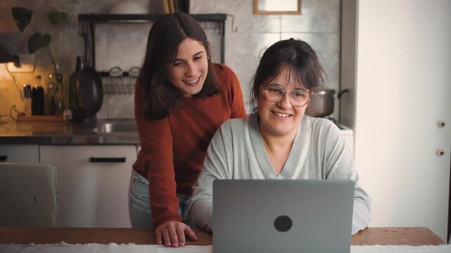 Young Latina woman at home looking at a laptop with her mother, representing family bonding, technology, digital learning, communication, and intergenerational connection.
