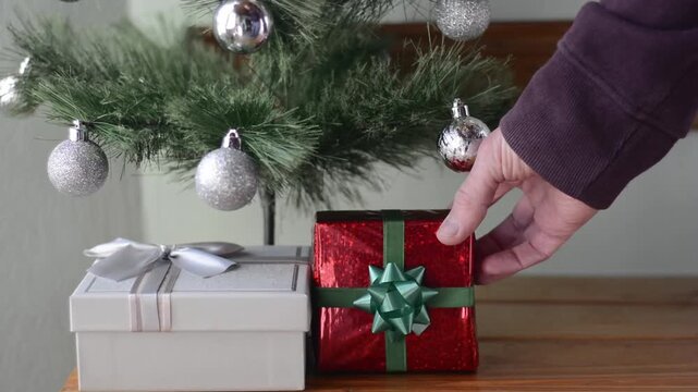 Man's hands placing wrapped gifts under a decorated Christmas tree