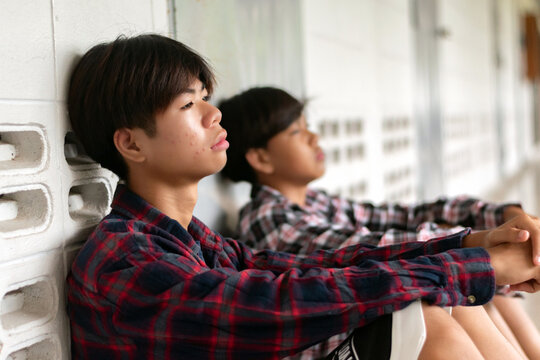 Two depressed teenage boys in plaid shirts sit on the floor of a school hallway, looking sad and lonely.