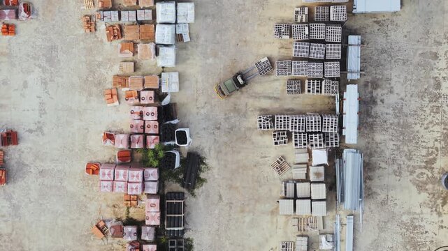 Aerial view of a forklift moving among organized stacks of construction materials and bricks in a supply yard in San Quirico d'Orcia, Tuscany, Italy.
