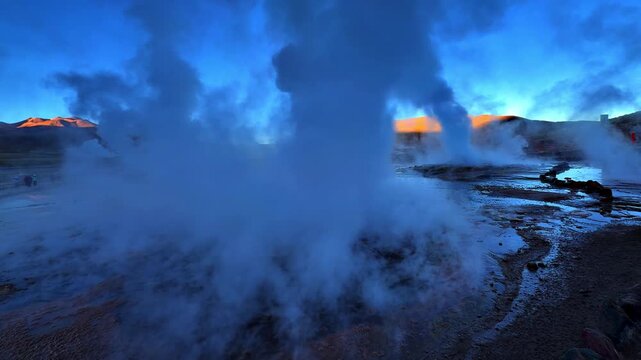 A geyser releases a tall column of water vapour in the Atacama Desert. The scene is filmed as a wide shot near Calama and Toconce in the Chilean Andes.