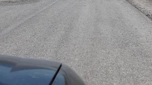 Dynamic, close-angle video showing the front of a car moving along a deteriorated asphalt road and swerving to avoid potholes.