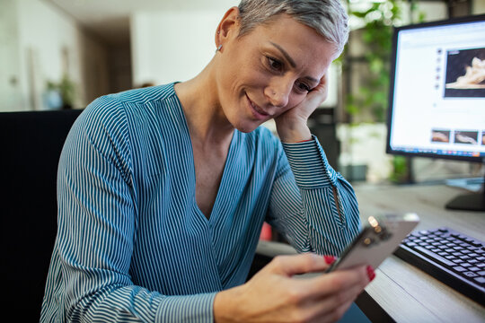 Smiling businesswoman using smartphone at office desk