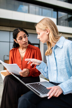 Two businesswomen collaborating with laptop and documents outside office