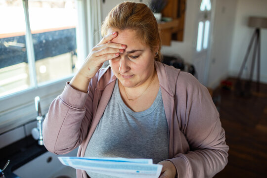 Stressed woman reading utility bills in home kitchen