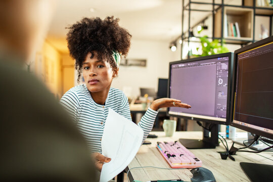 Female designer explaining project on dual monitors in home office