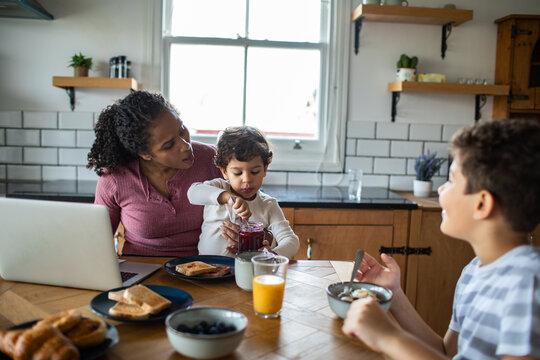 Mother helps kids make breakfast in home kitchen