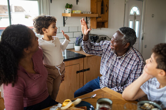 Multigenerational family high-fiving at breakfast in home kitchen