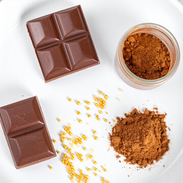 Chocolate bar and cocoa powder on white plate with golden sprinkles, overhead food composition evokes rich dessert preparation and sweet indulgence