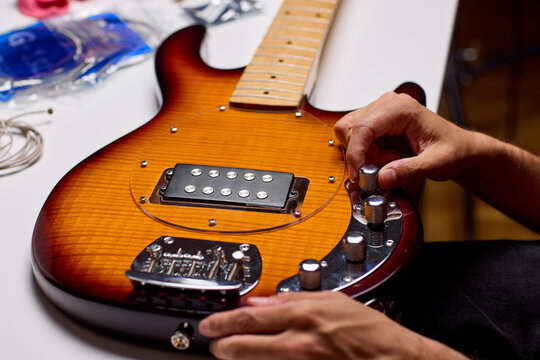 Close-up of hands adjusting control knobs on sunburst electric guitar resting on workbench in workshop