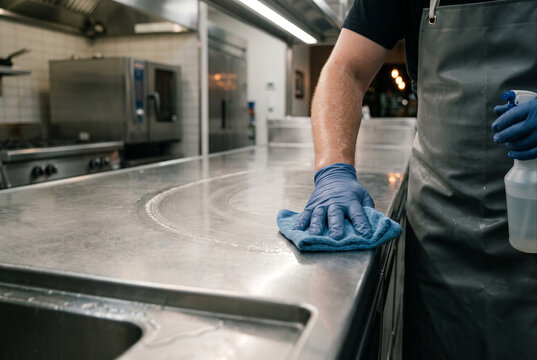 Worker sanitizing a stainless steel kitchen counter