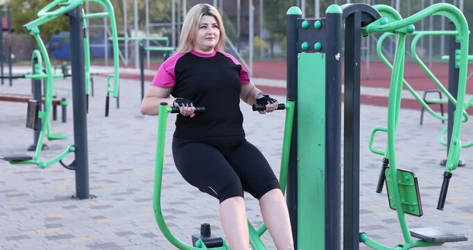 Overweight woman training on rowing machine at outdoor gym