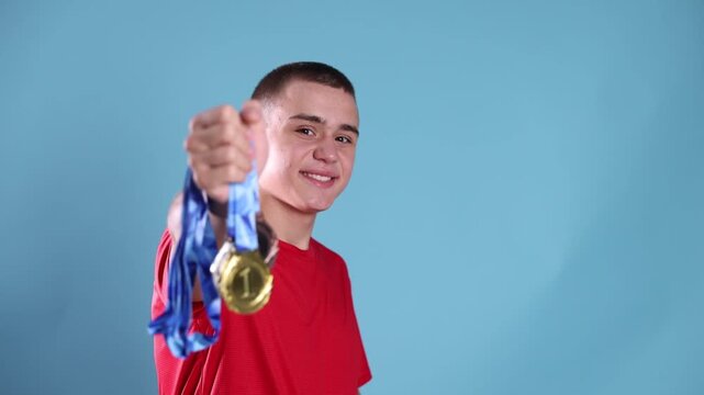 Happy teenage boy holding gold, silver and bronze medals against blue background, selective focus. Camera moving