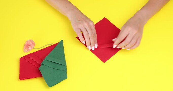 Woman folding red paper napkin to make silverware pouch at yellow table, above view